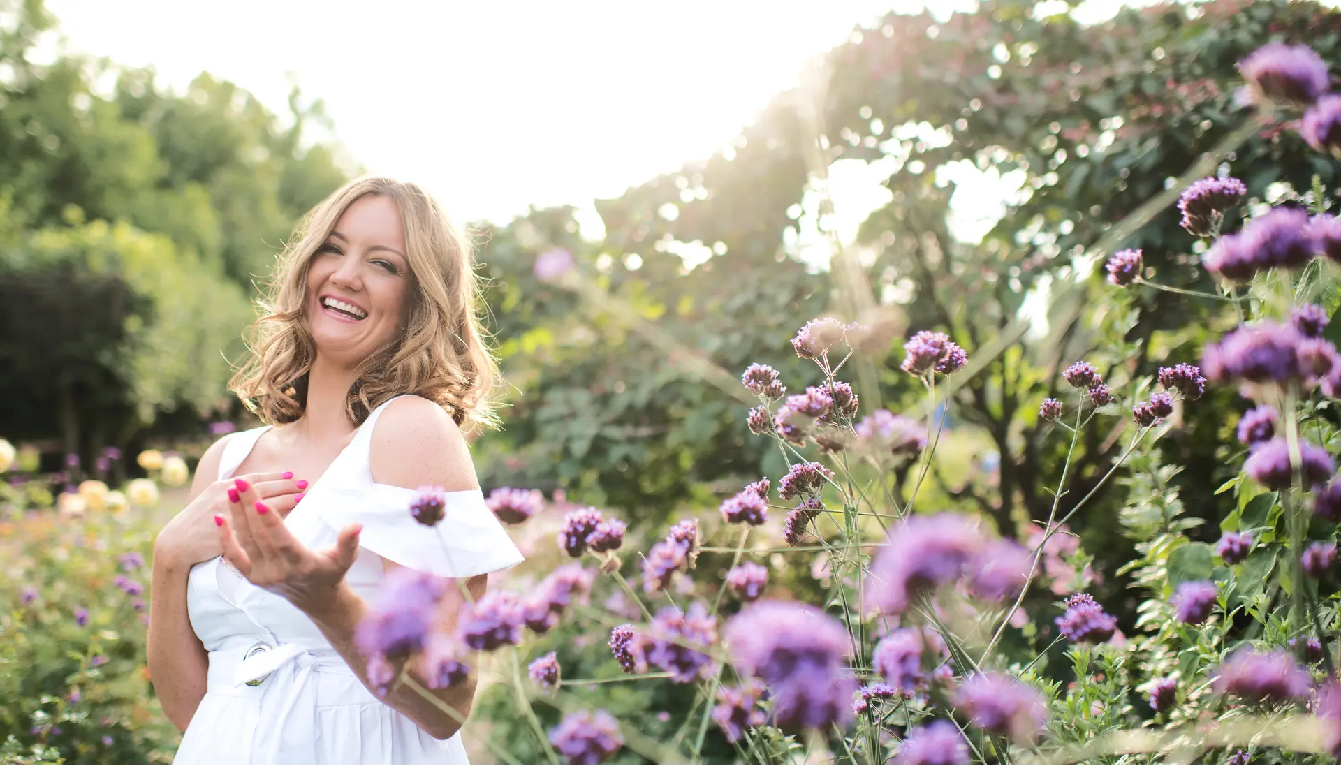 Jaimie Sarah standing outside with a white dress on and amongst purple flowers.