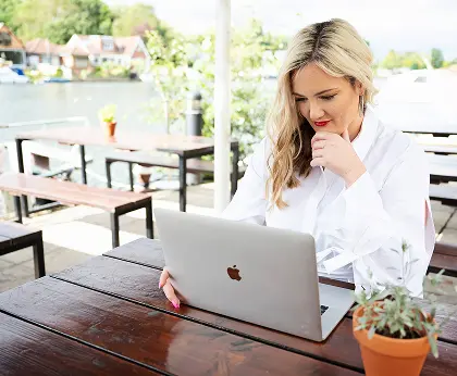 Jaimie Sarah wearing a white shirt sitting at her laptop putting together some plans for her clients by the river in Walton on Thames in Surrey.